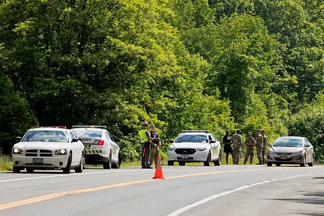 Military police and civilian first responders stand along Route 293 in response to a rollover of an armored personnel vehicle in which at least one person was killed, in Cornwall, N.Y.
